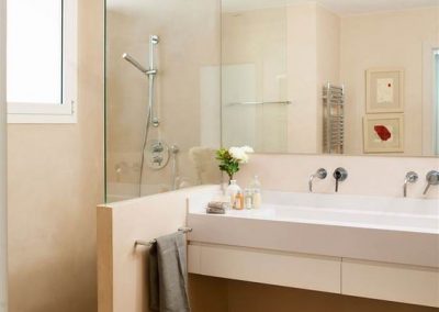 Baño en crema con ducha de obra separado del tocador con un murete rematado con un crtistal transparente a modo de mampara